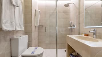 Een moderne badkamer met een douche met glazen wand, een wit toilet, een wastafel met spiegel en handdoeken op een rek.