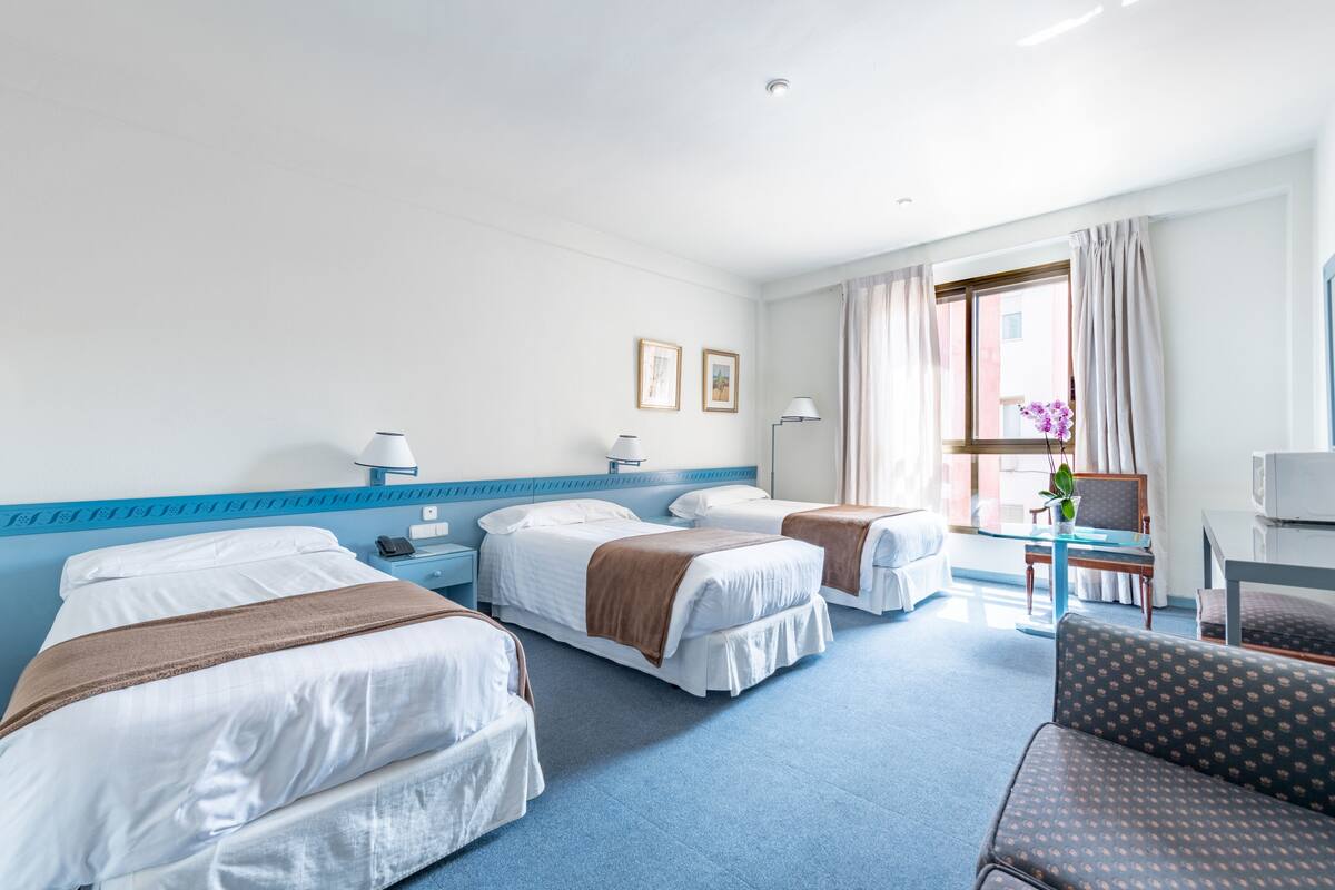 A hotel room with two beds, a desk, a chair, and a window with curtains.