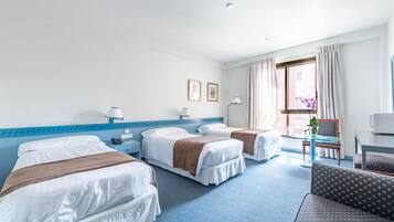 A hotel room with two beds, a desk, a chair, and a window with curtains.