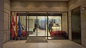A hotel entrance with glass doors, a reception desk, and flags outside.