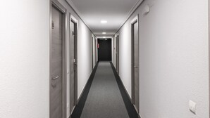 A long, narrow hotel corridor with doors on both sides, a grey carpet, and a white ceiling with a light fixture. - Hotel San Glorio (Santander)