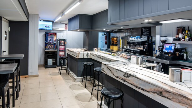 A modern bar area with a marble countertop, stools, a coffee machine, and a TV screen. - Hotel San Glorio (Santander)