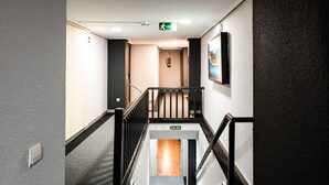 A hotel hallway with a staircase leading to an exit, a fire alarm, and a sign indicating the exit. - Hotel San Glorio (Santander)