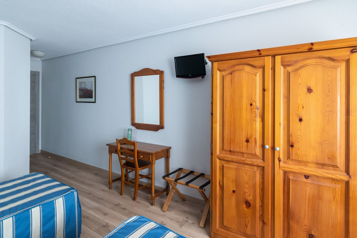 Una habitación con cama, escritorio, silla, televisor montado en la pared y armario.