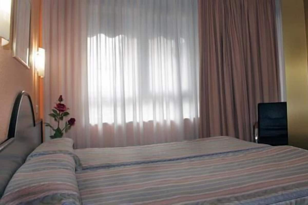 A hotel room with a bed, a chair, and a vase with flowers.