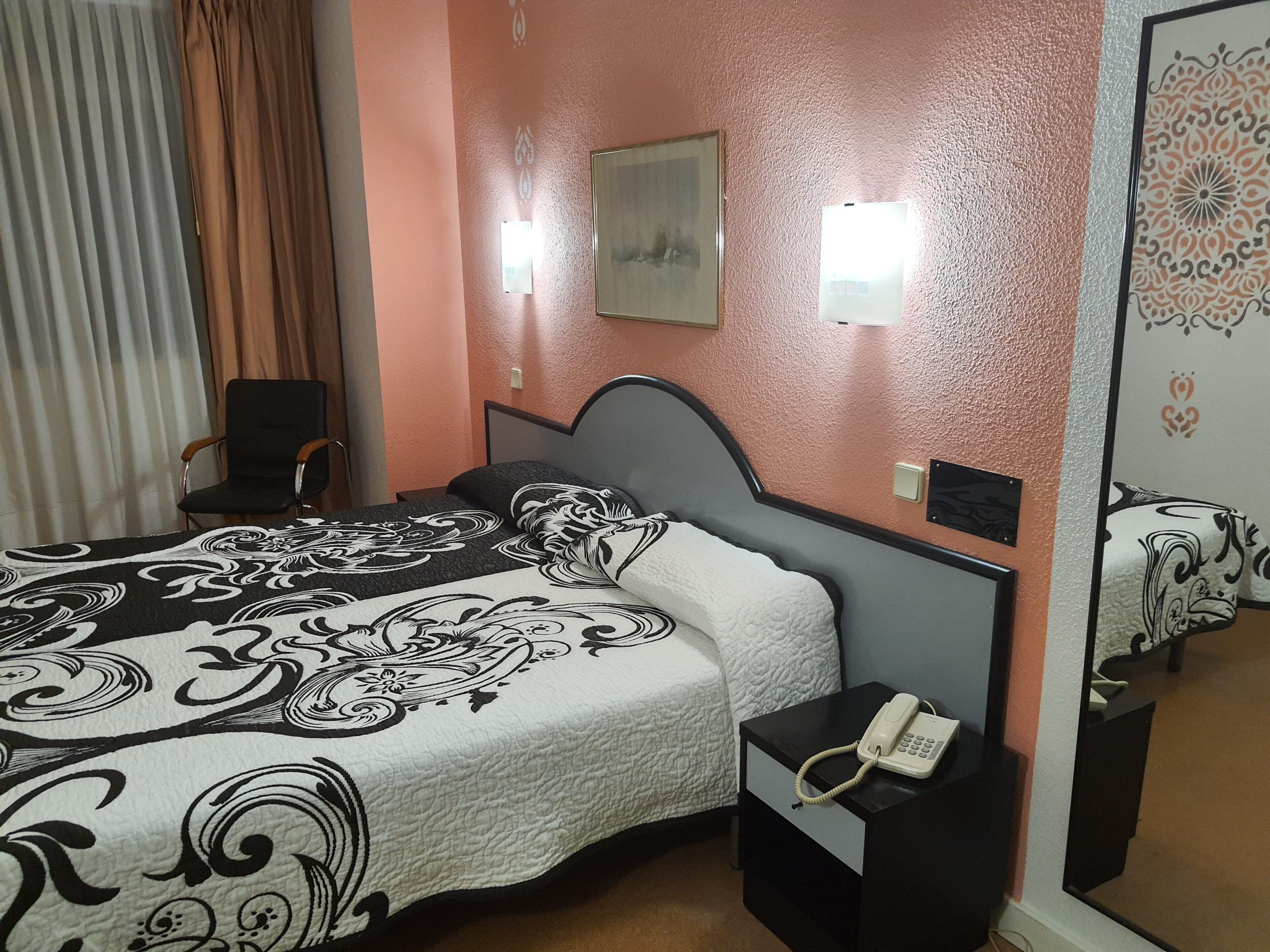 Habitación de hotel con cama, una silla, mesita de noche con teléfono e iluminación de pared.