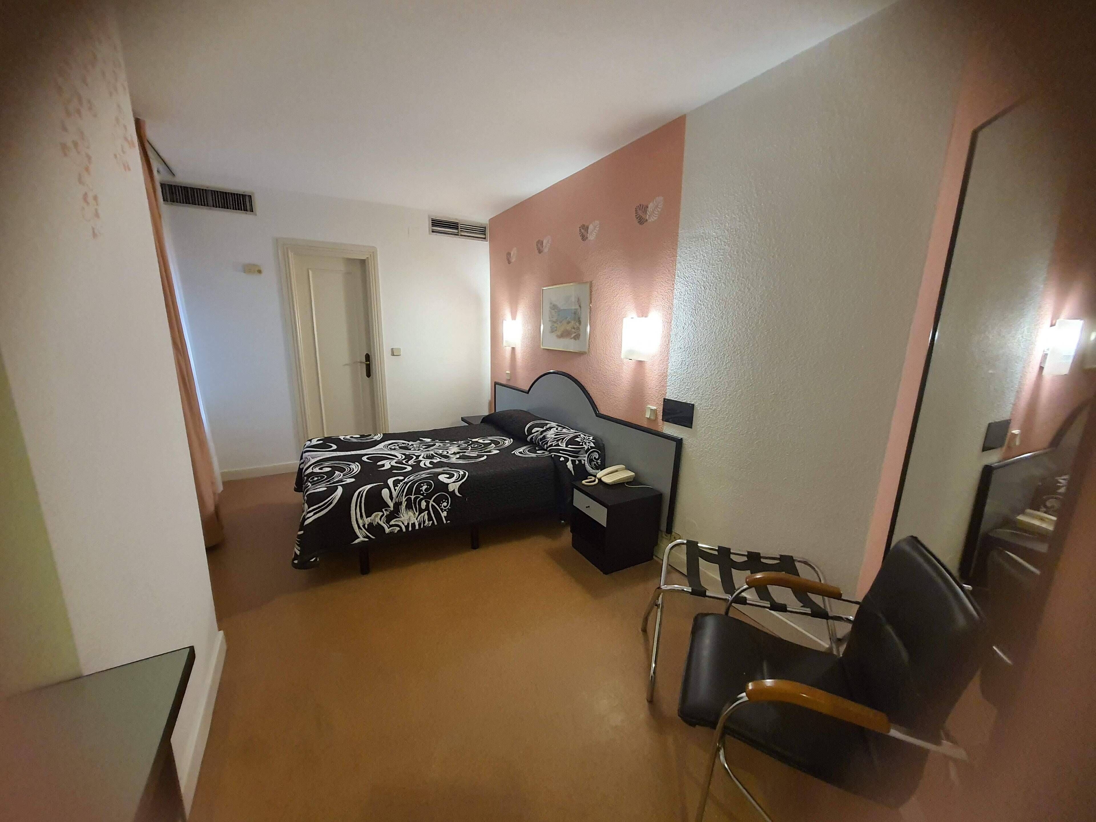 Un dormitorio con cama, mesita de noche, silla y puerta.