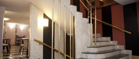 A modern interior with a marble staircase, a dining area with chairs, and a patterned wall.