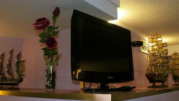 Un televisor sobre un mueble, con un modelo de barco y un jarrón de flores en un estante.