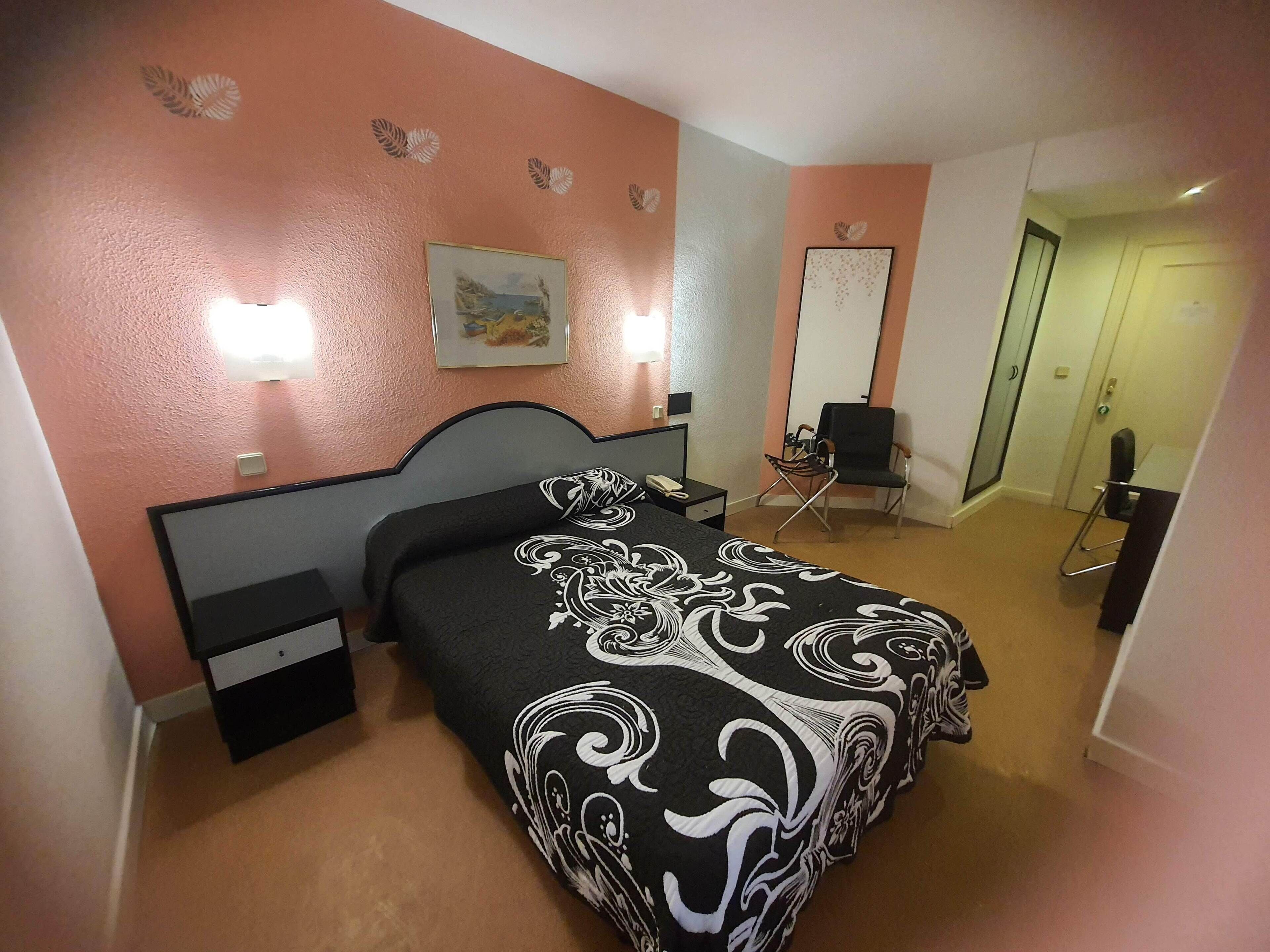 A hotel room with a bed, bedside tables, a desk, a chair, and a door.