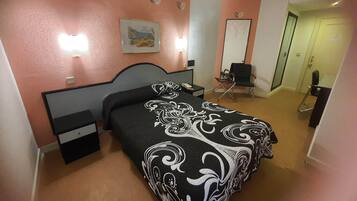 A hotel room with a bed, bedside tables, a desk, a chair, and a door.