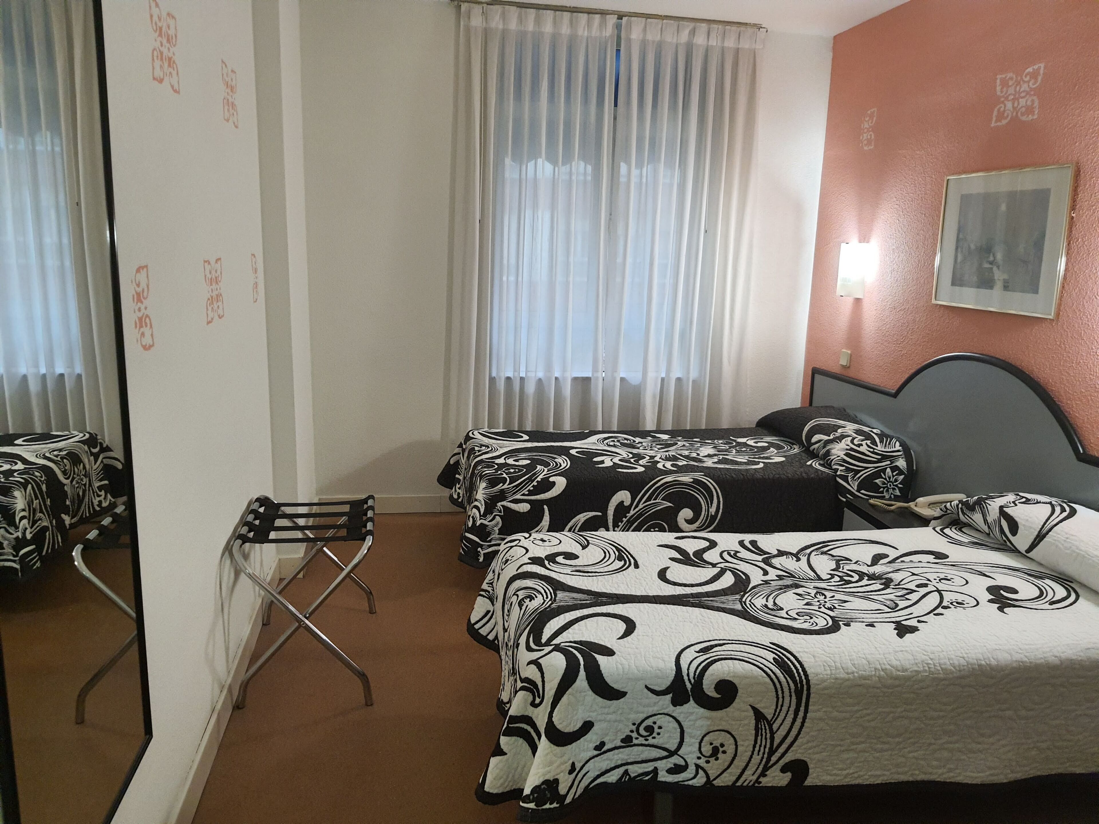 Habitación de hotel con dos camas, una silla, un ventanal con cortinas y un cuadro colgado en la pared.