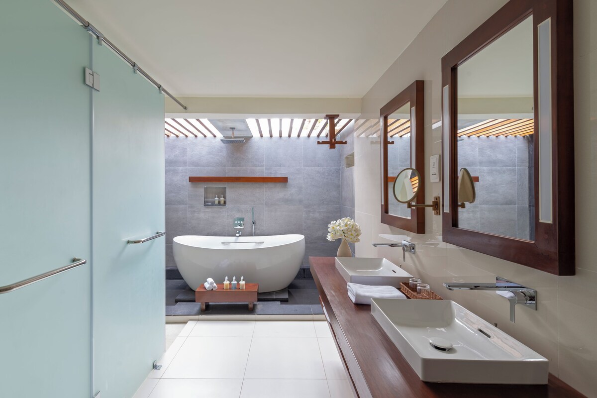 A modern bathroom with a freestanding bathtub, a vanity with two sinks, a mirror, and a wooden shelf.