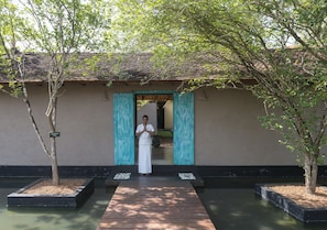 A person standing at the entrance of a building with a tiled roof and a pathway leading to the entrance.