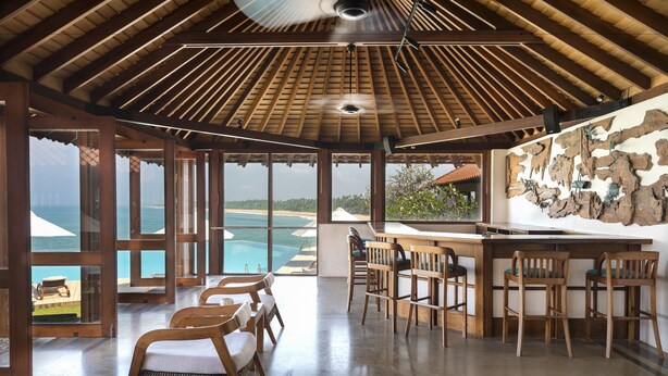 Amplia habitación con techo de madera, una zona de bar con taburetes y vistas al océano.
