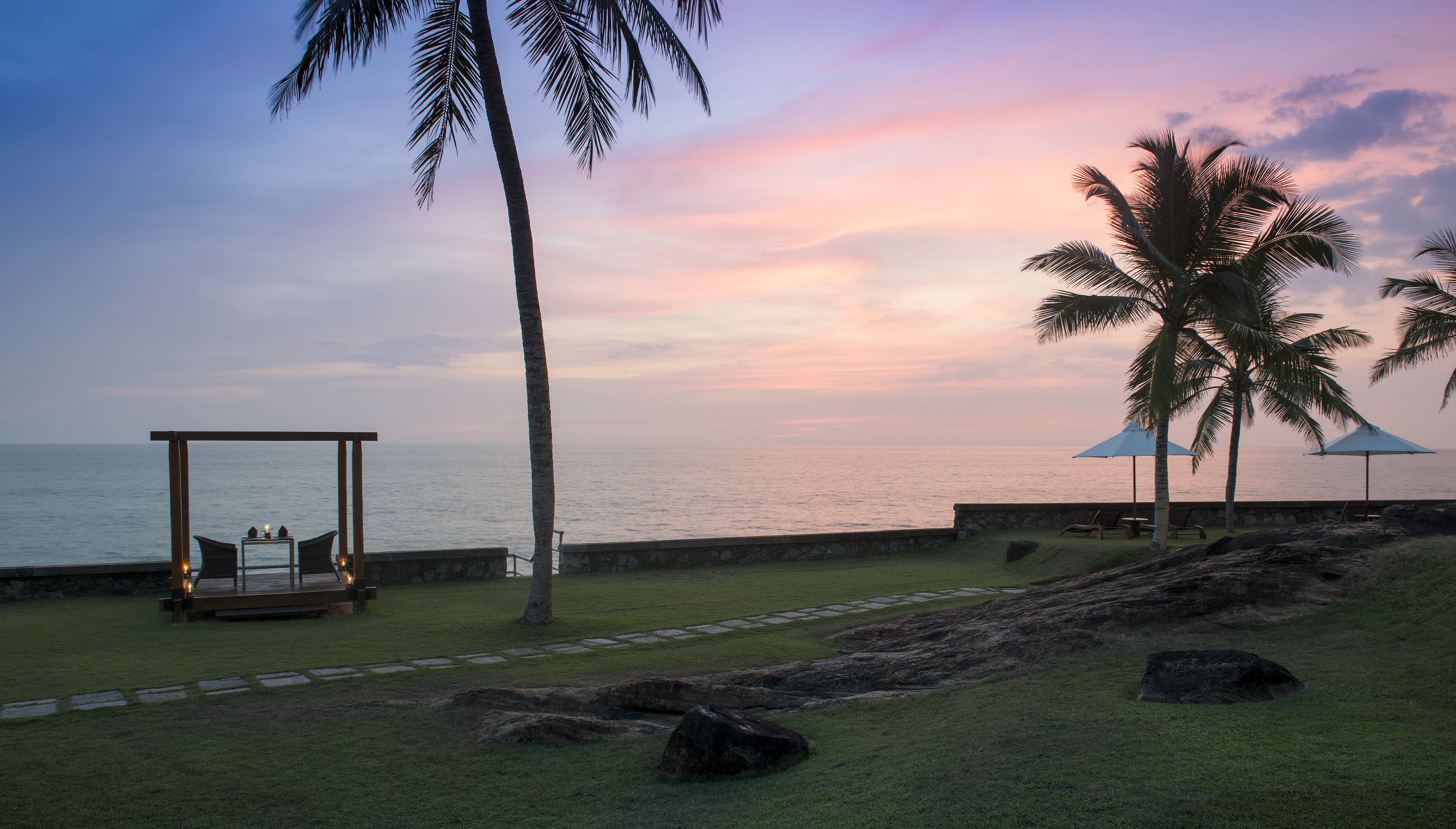 A beachside setting with a wooden deck, lounge chairs, and a palm tree.