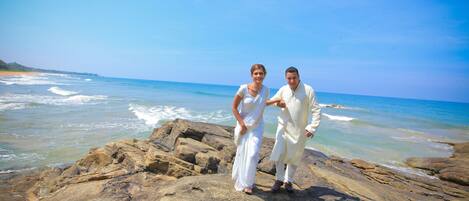 A couple standing on a rocky beach with the ocean in the background.