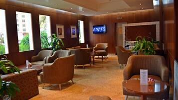 A hotel lobby with multiple seating areas, a television, and large windows offering views of the outside.