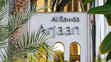 La façade extérieure de l’hôtel Al Rawda Arjaan, avec son panneau indicateur, est entourée de verdure.