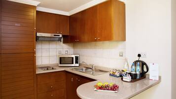 A compact kitchen with wooden cabinets, a microwave, a coffee maker, and a fruit bowl on the counter.