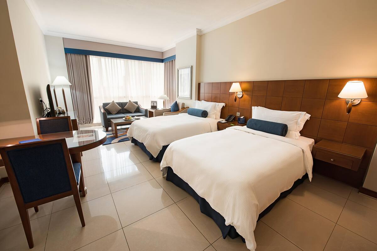 Ein Hotelzimmer mit zwei Betten, einem Schreibtisch, einem Stuhl, einem Sofa und einem Esstisch.