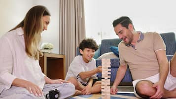 Une famille joue à un jeu de société à l’intérieur, avec un canapé et une petite table en arrière-plan.