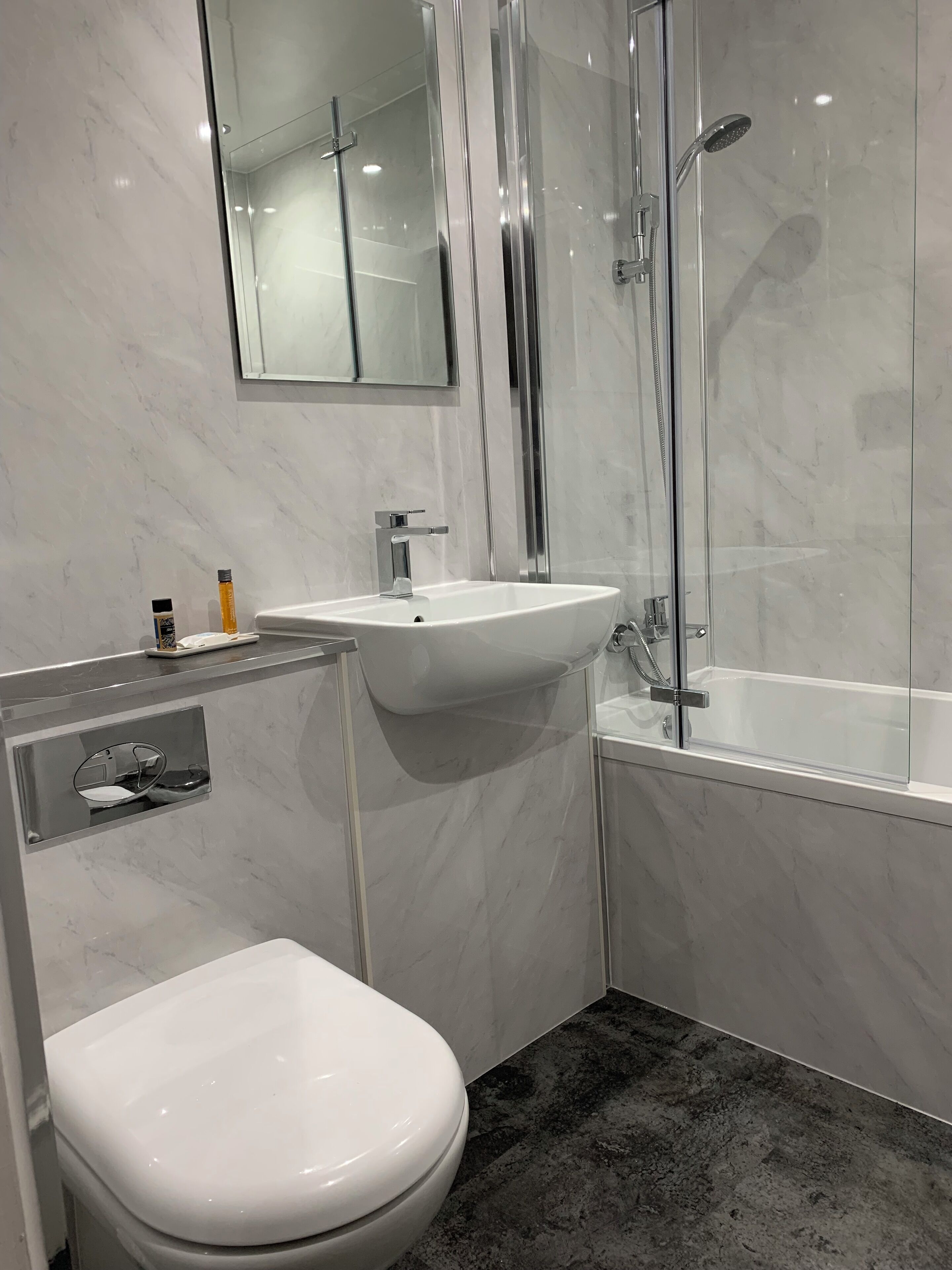 Un baño moderno con inodoro blanco, lavamanos y zona de ducha con mampara de vidrio.