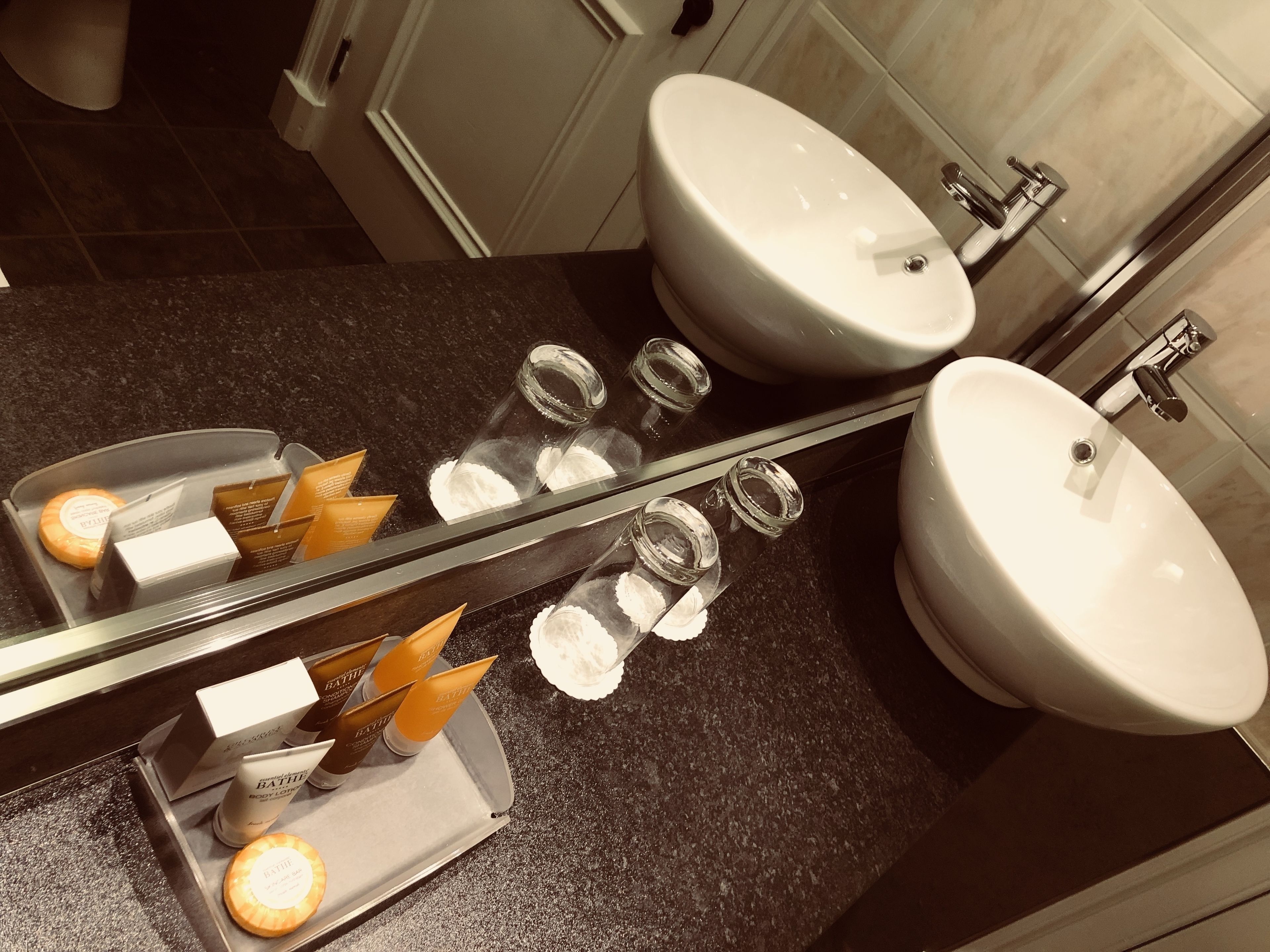 A bathroom with two sinks, a mirror, and toiletries on the counter.