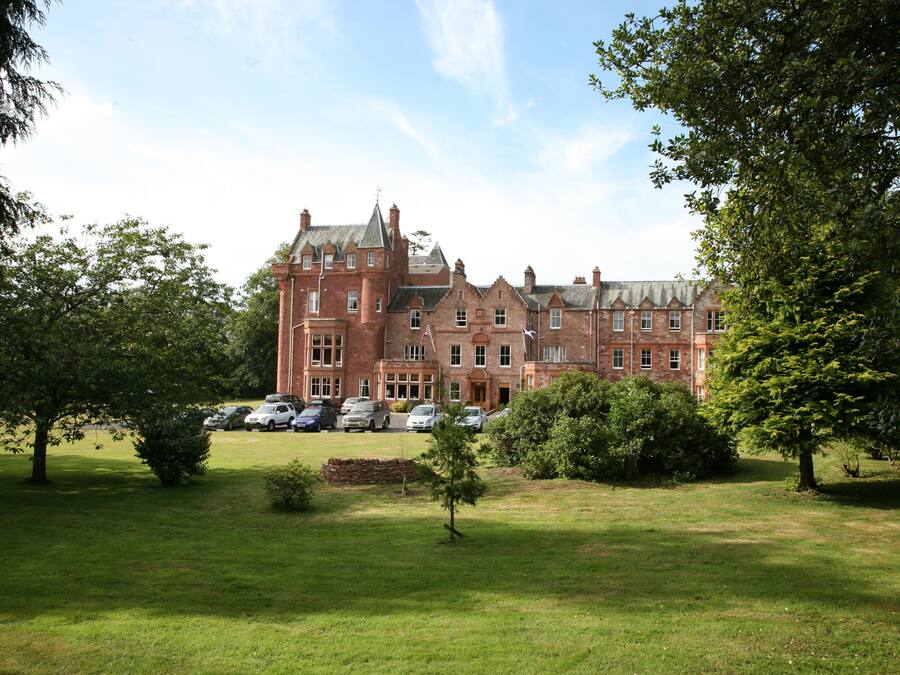A large, historic brick building with multiple windows and a well-maintained lawn in front.