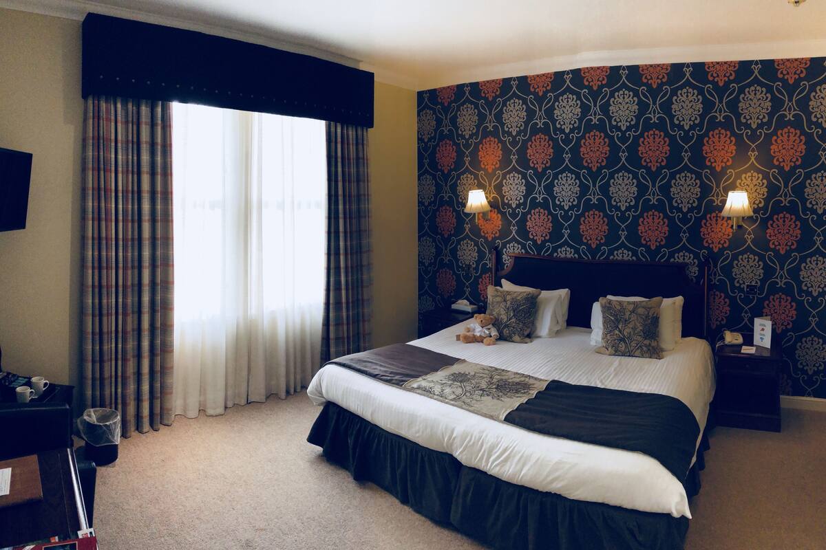 A hotel room with a large bed, two bedside lamps, a television, and a window with curtains.