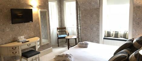 Una habitación de hotel con cama, escritorio, silla, televisión y ventana con cortinas.