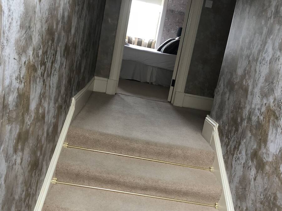 A carpeted staircase with a handrail, leading to a room with a window and a bed.