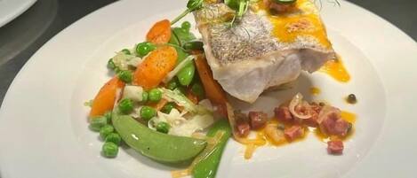 A plate of food with a fish fillet, peas, carrots, and a sauce.