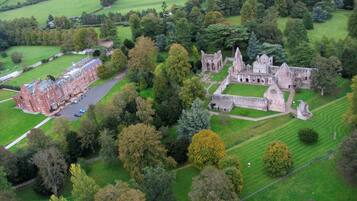 An aerial view of a historic building complex with a large courtyard, surrounded by lush greenery and fields.