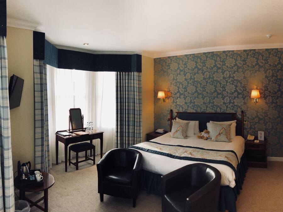 Ein Hotelzimmer mit Bett, zwei Stühlen, einem Schreibtisch und einem fenster mit Vorhängen.