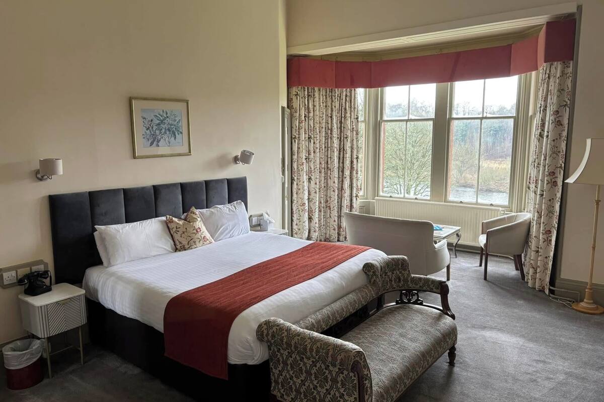 A hotel room with a large bed, a desk, a chair, and a window with curtains.