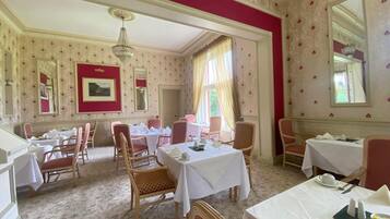 A dining room with multiple tables and chairs, a chandelier, and patterned wallpaper.