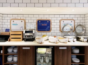 A breakfast station with a coffee machine, bowls of cereal, and a milk dispenser.