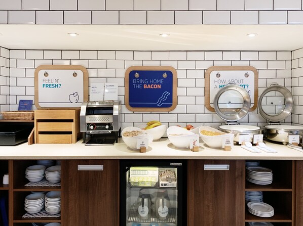 A breakfast station with a coffee machine, bowls of cereal, and a milk dispenser. - Holiday Inn Express London Victoria by IHG (London)
