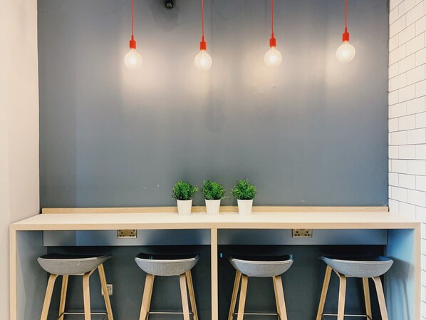 A modern kitchen with a grey backsplash, three bar stools, and three potted plants. - Holiday Inn Express London Victoria by IHG (London)