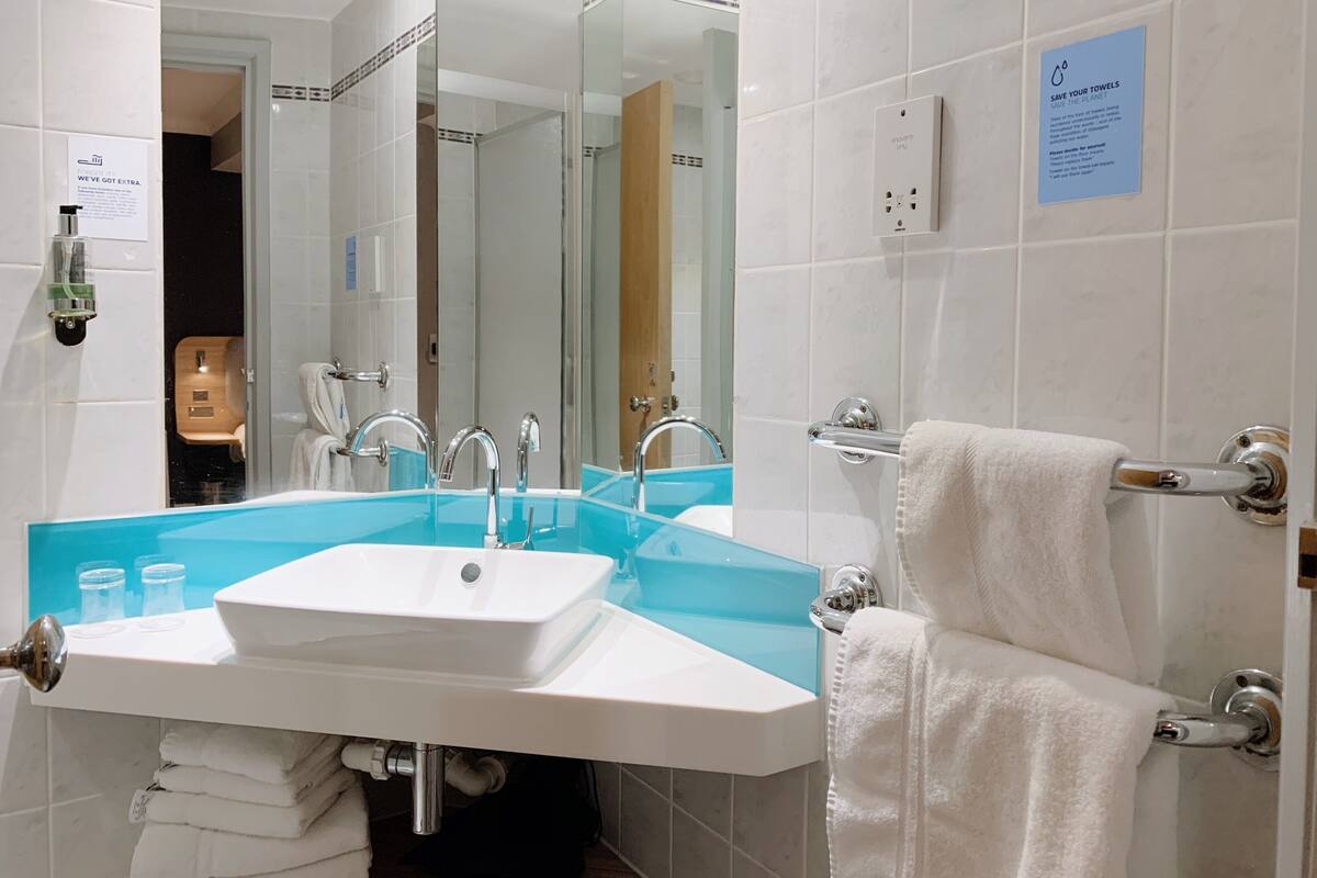 Un baño con un lavabo blanco, dos grifos, un espejo y un perchero para toallas.