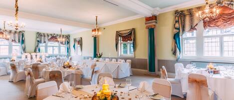 A banquet hall with round tables, chandeliers, and floral decorations.