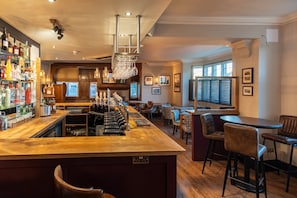 A bar area with a long counter, multiple stools, and a variety of bottles.