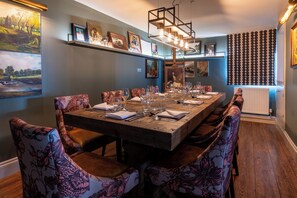 A dining area with a long wooden table, floral upholstered chairs, and framed artwork on the walls. - Colwall Park Hotel (Malvern)