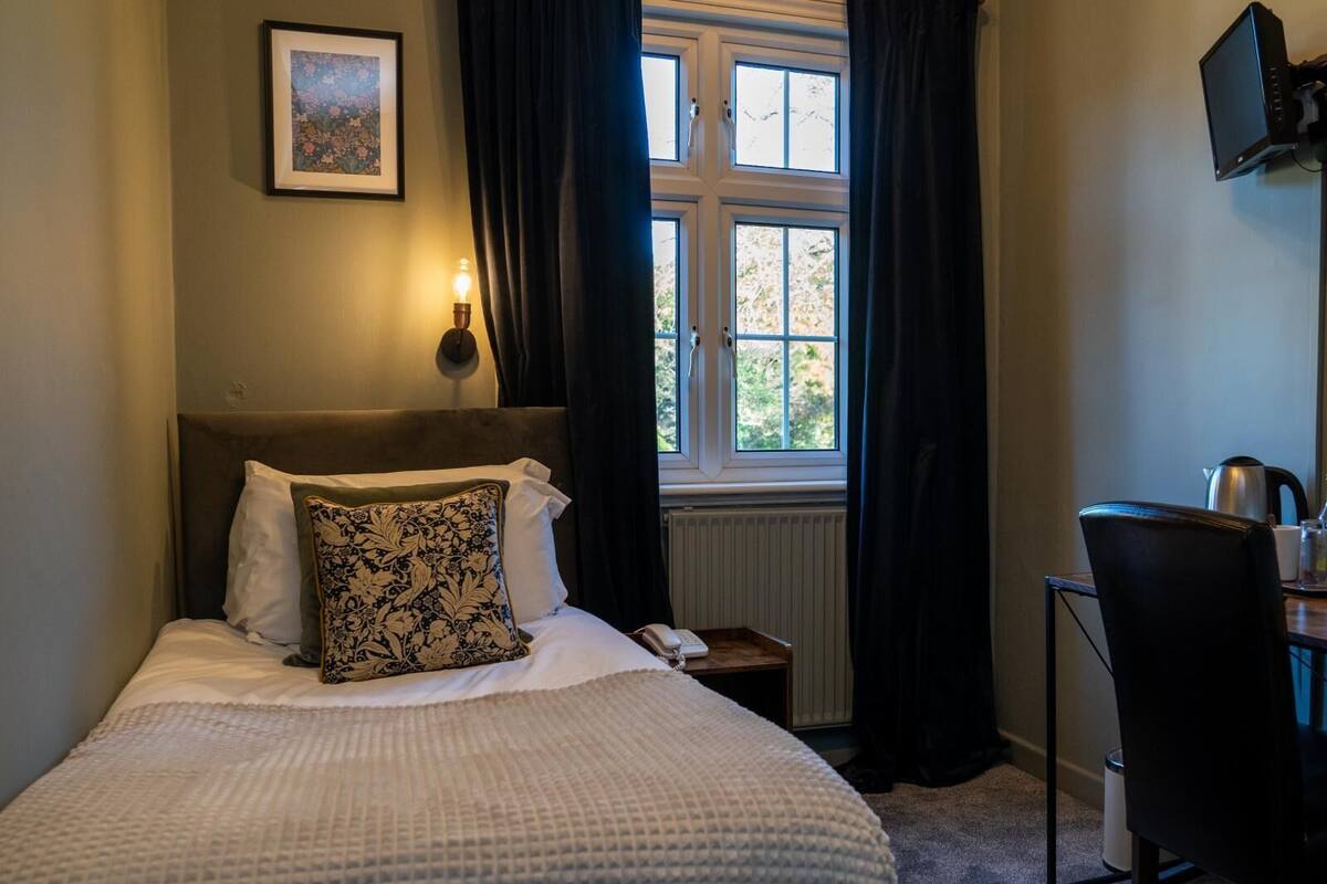 Une chambre à coucher avec un lit, une table de chevet avec une lampe, un bureau avec une chaise et une fenêtre avec des rideaux.