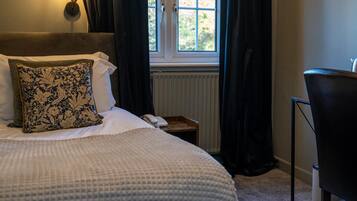 A neatly made bed with a patterned pillow, a bedside table with a phone, and a chair.