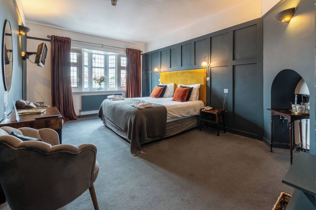Une chambre à coucher comprenant un lit, un bureau, une chaise, une fenêtre avec des rideaux et une lampe fixée au mur.