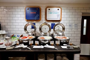 A buffet setup with labeled food stations, including a 'Bring Home the Bacon' and 'How About a Hot Start?' sign, and various utensils and condiments. - Holiday Inn Express Glenrothes by IHG (Glenrothes)