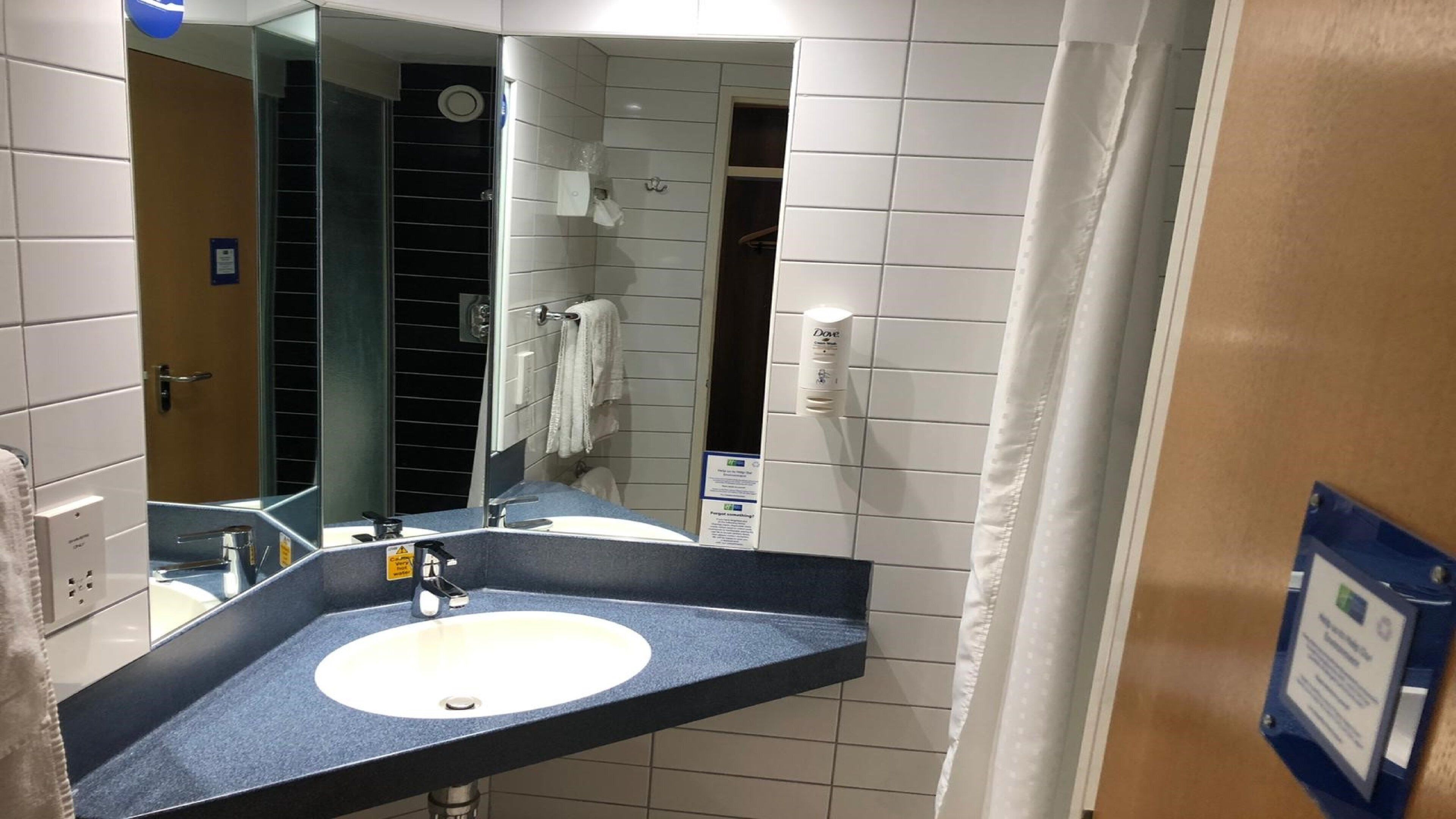 Un baño con lavamanos, espejo, toallero y zona de ducha.