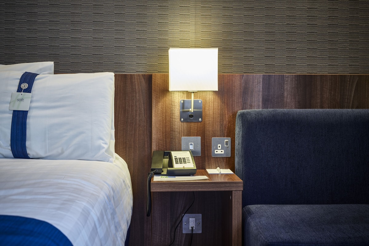 A hotel room with a bed, a desk with a telephone, and a chair.